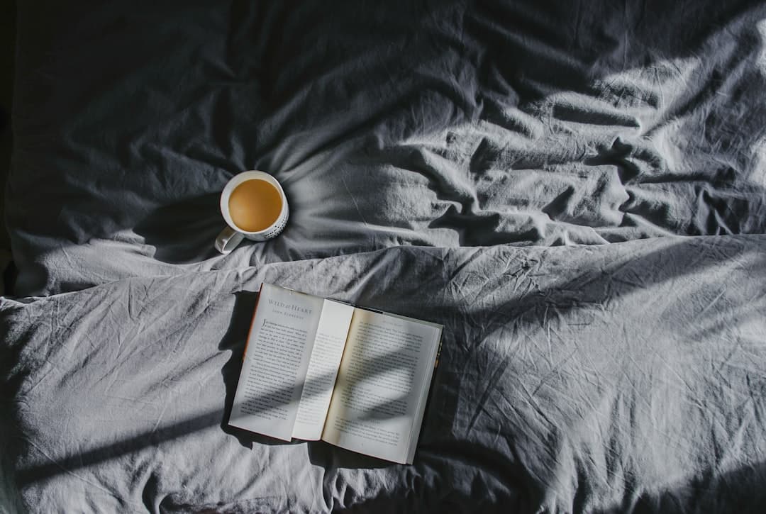 Koffiekop naast een boek op een bed met grijze lakens